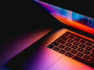 A laptop screen illuminated, red light reflecting on the keyboard.