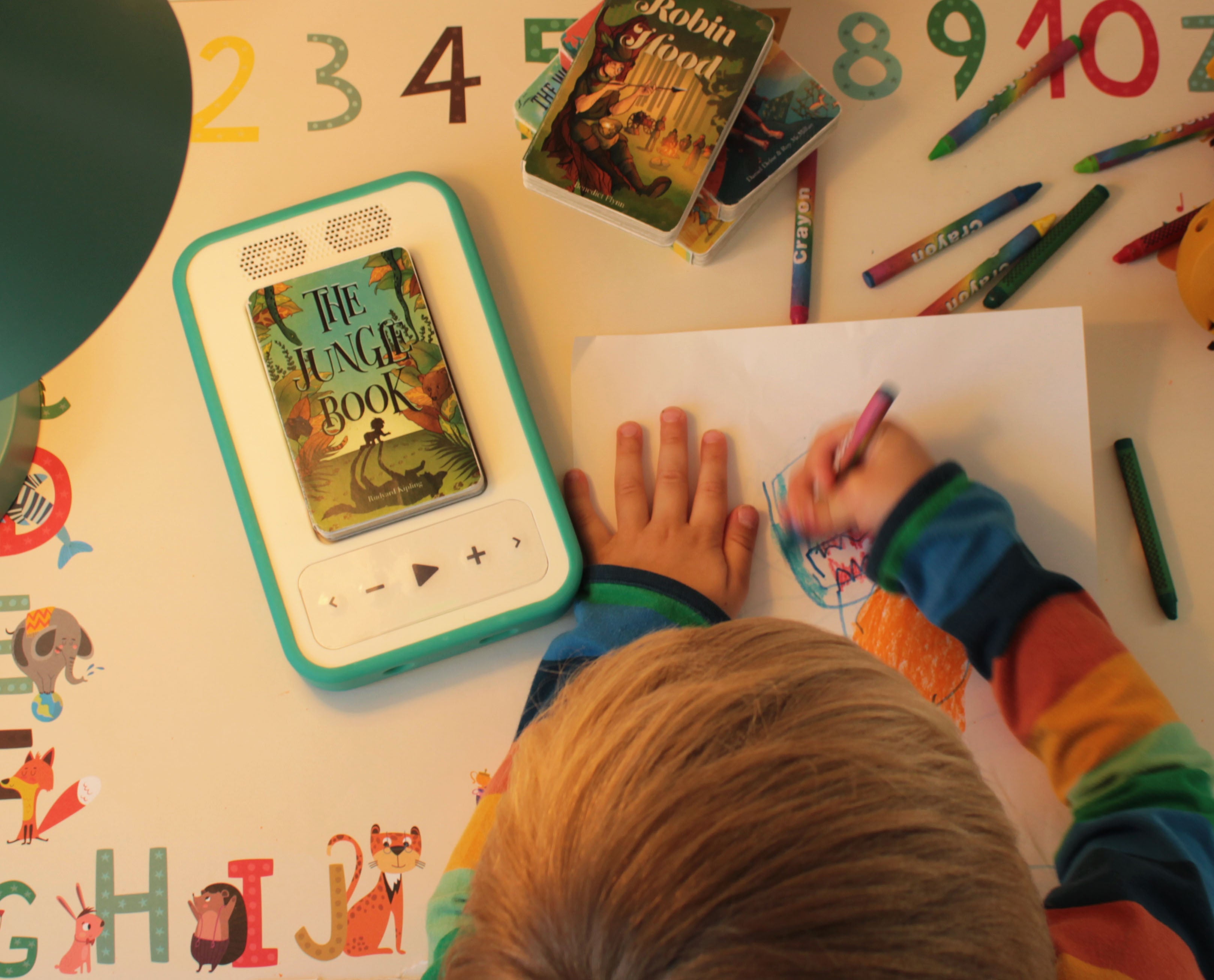 Viewed from above, a child draws while listening to The Jungle Book audiobook.