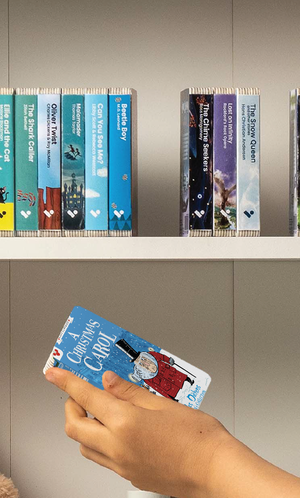 A hand taking A Christmas Carol audiobook from a shelf of Voxblock audiobooks