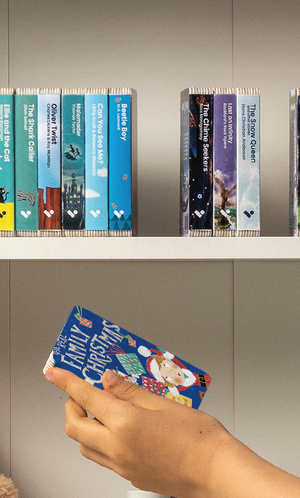 A hand taking The Real Family Christmas audiobook from a shelf of Voxblock audiobooks