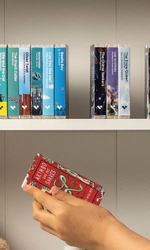 A hand taking the Akimbo and the Snakes audiobook from a shelf of Voxblock audiobooks