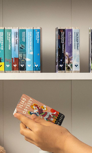 A hand taking the Homer's Iliad and the Odyssey: Two of the Greatest Stories Ever Told audiobook from a shelf of Voxblock audiobooks