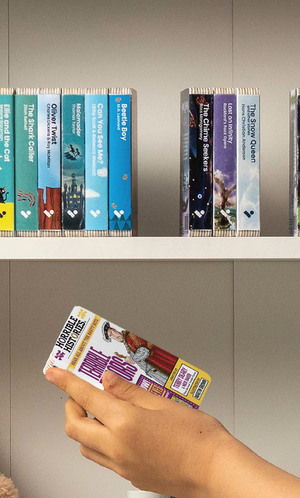 A hand taking the Horrible Histories: Terrible Tudors audiobook from a shelf of Voxblock audiobooks
