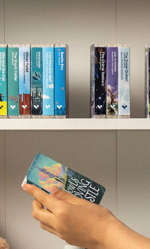 A hand taking the Howl’s Moving Castle audiobook from a shelf of Voxblock audiobooks