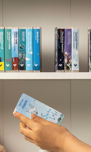 A hand taking the Swan Lake audiobook from a shelf of Voxblock audiobooks