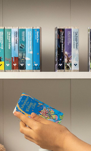 A hand taking The Adventures of the Wishing Chair audiobook from a shelf of Voxblock audiobooks