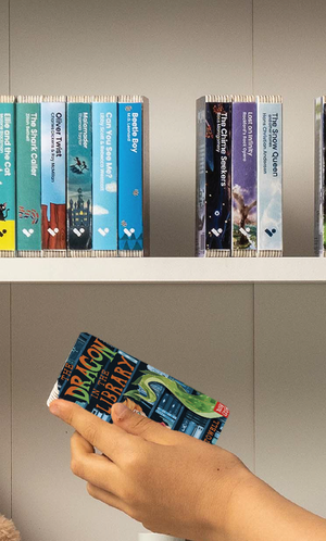 A hand taking The Dragon in the Library audiobook from a shelf of Voxblock audiobooks