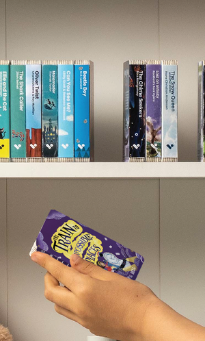A hand taking The Train to Impossible Places audiobook from a shelf of Voxblock audiobooks