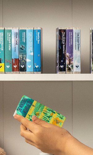 A hand taking The Wonderful Wizard of Oz audiobook from a shelf of Voxblock audiobooks
