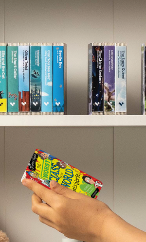 A hand taking The Worst Class in the World Gets Worse audiobook from a shelf of Voxblock audiobooks