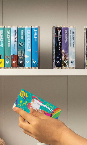 A hand taking the Unicorn Academy: Scarlett and Blaze audiobook from a shelf of Voxblock audiobooks
