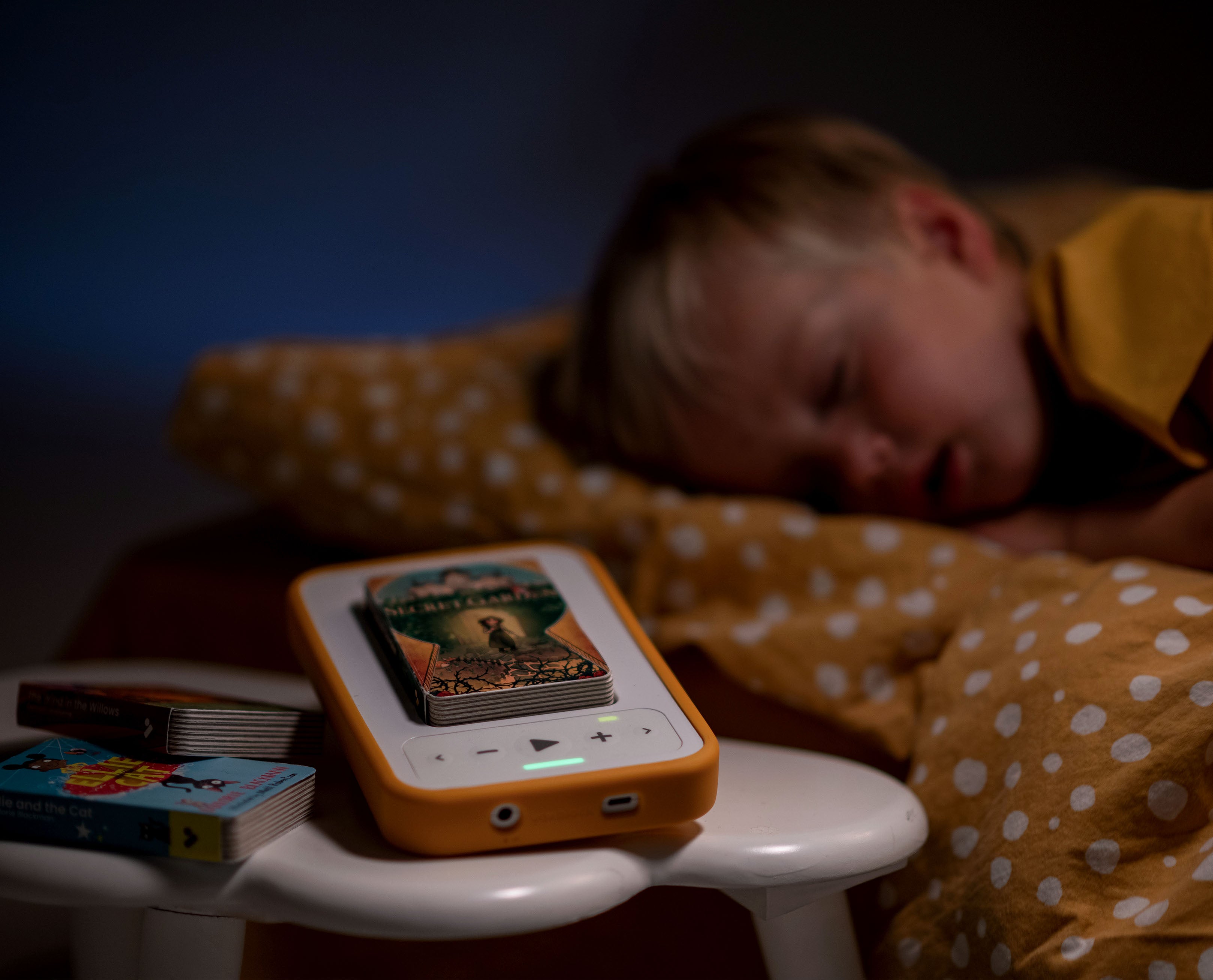 The Secret Garden audiobook and audiobook player sit on a bedside table beside a sleeping child.