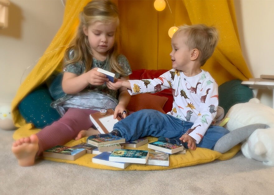 Two children sitting on the floor swap audiobooks. A pile of Voxblock audiobooks sits in front of them.