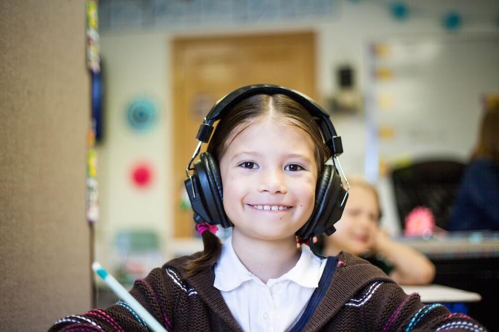 A young girl wears headphones as she learns by listening to an audiobook in the classroom