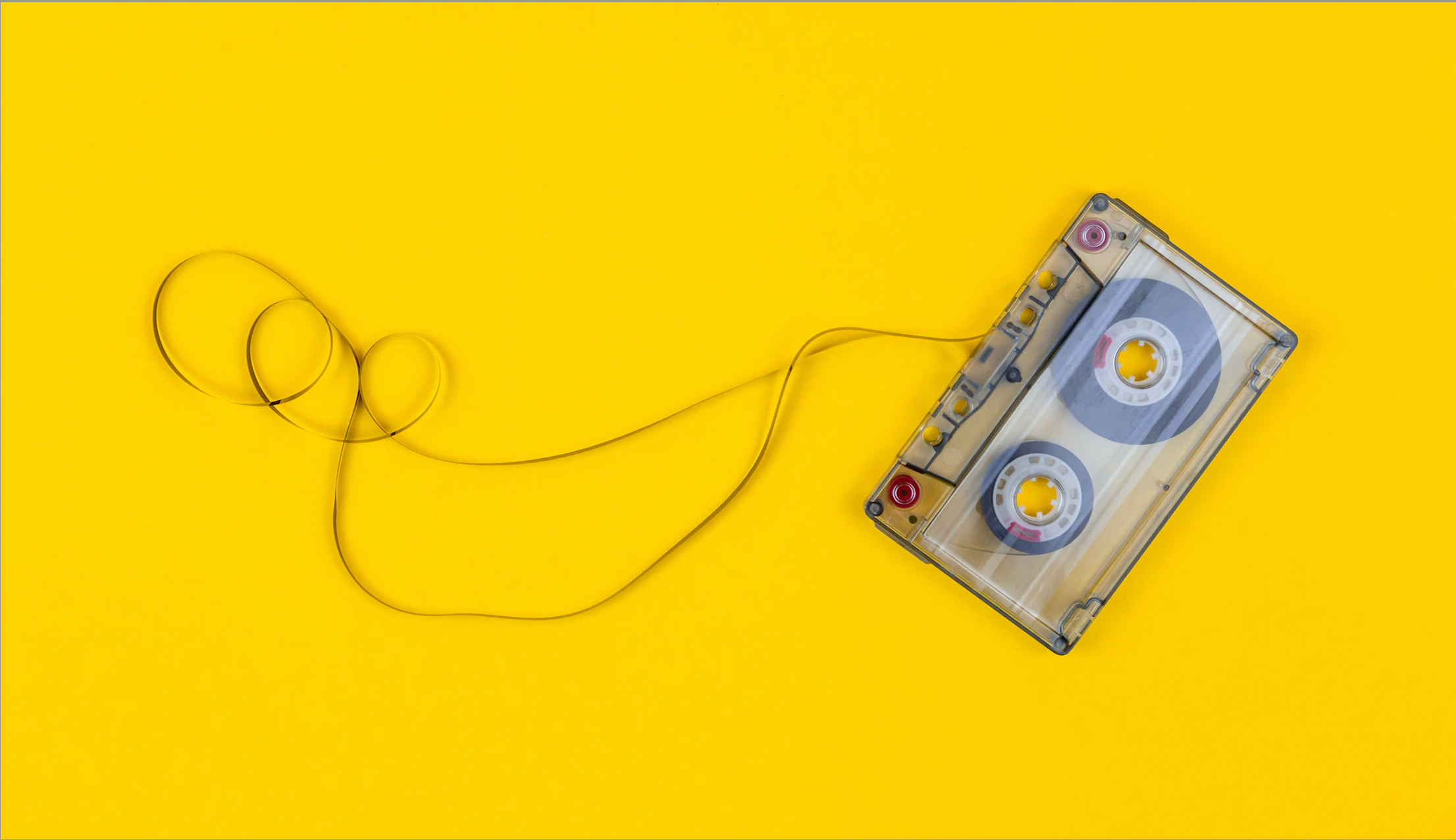 A cassette tape with the ribbon unravelled lies flat on a yellow background.