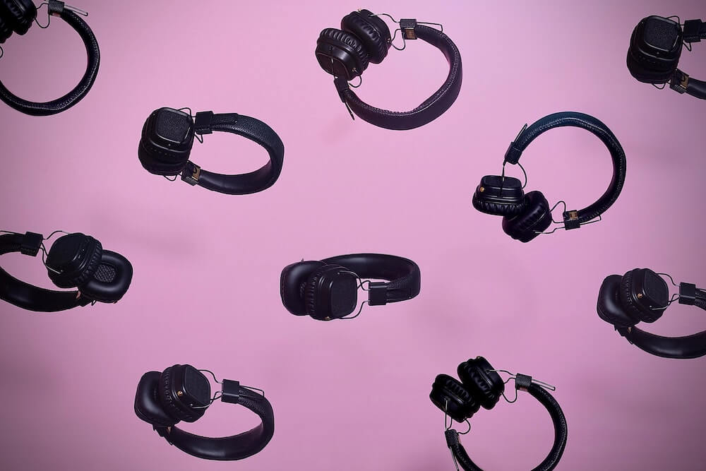 Headphones, as used for listening to audiobook apps, arranged in a repeated pattern on a pink background.