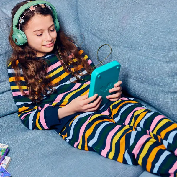 Girl in colorful pajamas sitting on a blue couch using an audiobook player.