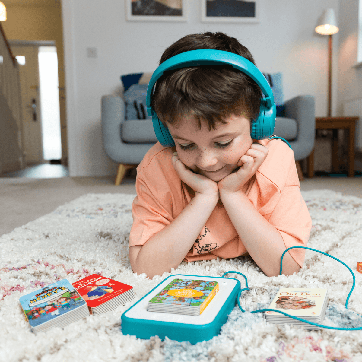 Boy lying on a rug with teal headphones, a Voxblock player and two audiobooks