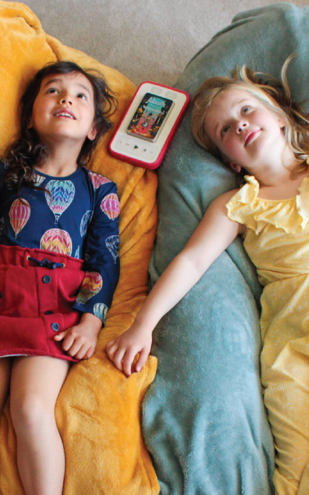 two girls relaxing listening to Alice's Adventures in Wonderland audiobook on a Voxblock screen-free audiobook player