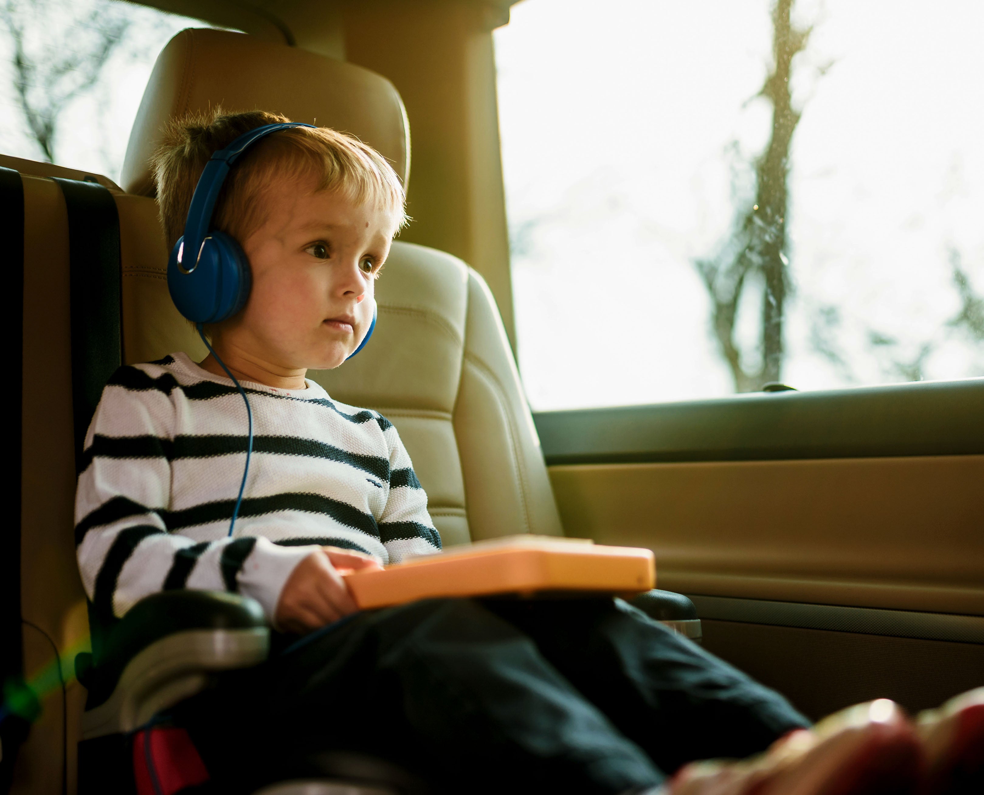 A young boy wears headphones and listens to an audiobook in the car using the Voxblock audiobook player.