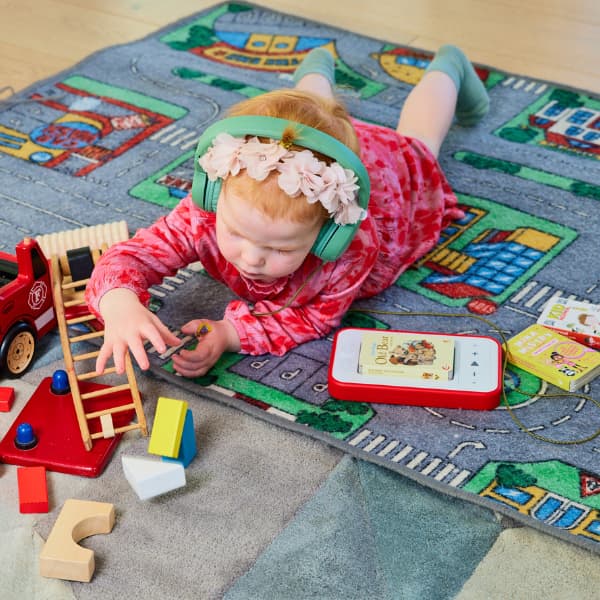 little girl playing with toys and listening to a Voxblock on a rug