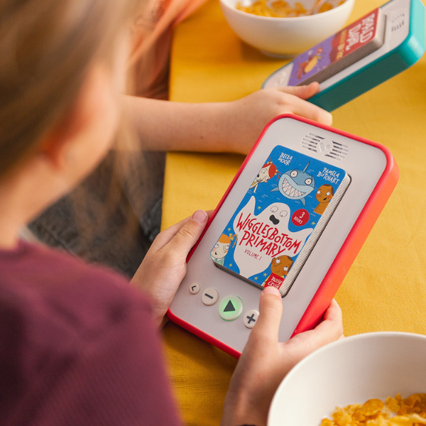 Child using a Voxblock device with Wigglesbottom Primary audiobook inserted on a yellow table.