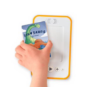 A hand holding the audiobook card for Dinosaurs beside a Voxblock audiobook player
