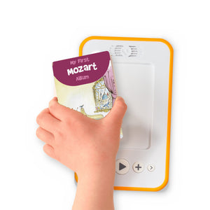 A hand holding the audiobook card for My First Mozart Album beside a Voxblock audiobook player