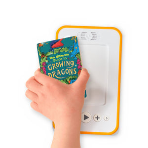 A hand holding the audiobook card for The Ultimate Guide to Growing Dragons beside a Voxblock audiobook player