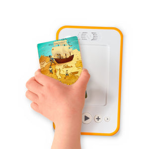A hand holding the audiobook card for Treasure Island beside a Voxblock audiobook player