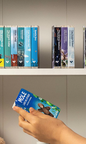 A hand taking A Mole Like No Other audiobook from a shelf of Voxblock audiobooks