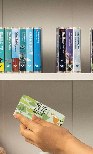 A hand taking the Aesop's Fables Reimagined audiobook from a shelf of Voxblock audiobooks