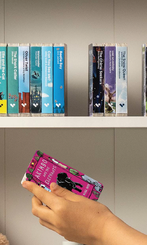A hand taking the Akimbo and the Elephants audiobook from a shelf of Voxblock audiobooks