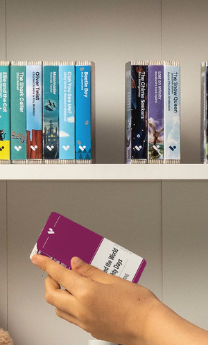 A hand taking the Around the World in Eighty Days audiobook from a shelf of Voxblock audiobooks