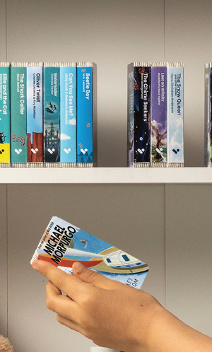 A hand taking the Kensuke's Kingdom audiobook from a shelf of Voxblock audiobooks
