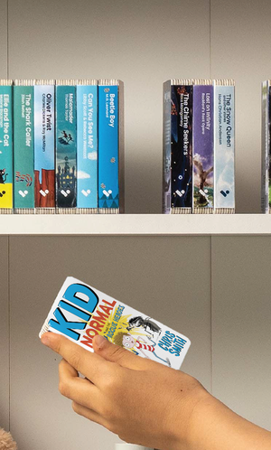 A hand taking the Kid Normal and the Rogue Heroes audiobook from a shelf of Voxblock audiobooks