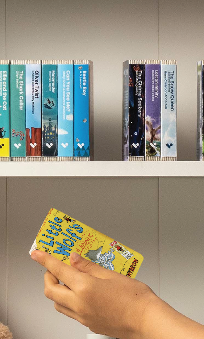 A hand taking the Little Wolf's Book of Badness audiobook from a shelf of Voxblock audiobooks