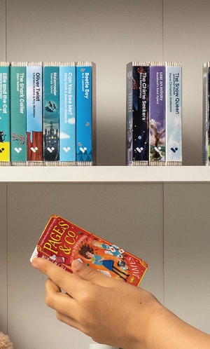 A hand taking the Pages & Co.: Tilly and the Bookwanderers audiobook from a shelf of Voxblock audiobooks
