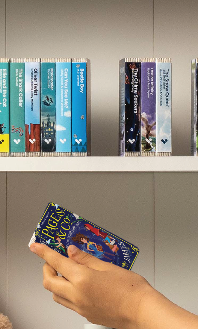 A hand taking the Pages & Co.: Tilly and the Lost Fairy Tales audiobook from a shelf of Voxblock audiobooks