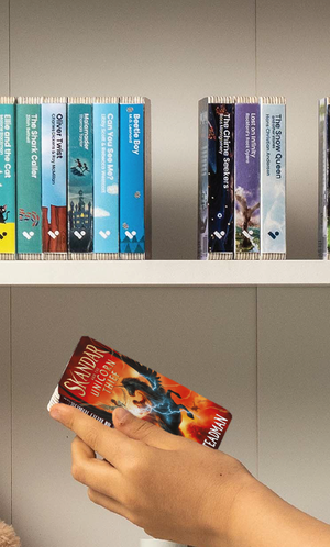A hand taking the Skandar and the Unicorn Thief audiobook from a shelf of Voxblock audiobooks