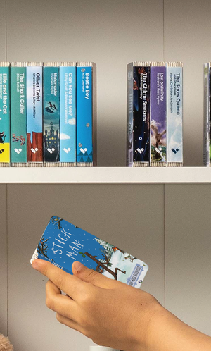 A hand taking the Stick Man audiobook from a shelf of Voxblock audiobooks