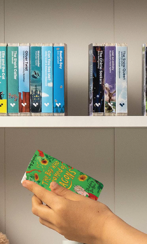 A hand taking The Boy Who Dreamed of Dragons audiobook from a shelf of Voxblock audiobooks