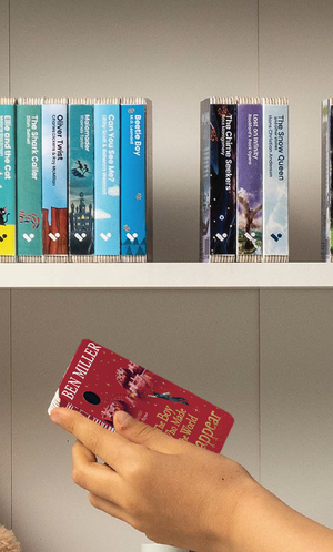 A hand taking The Boy Who Made the World Disappear audiobook from a shelf of Voxblock audiobooks