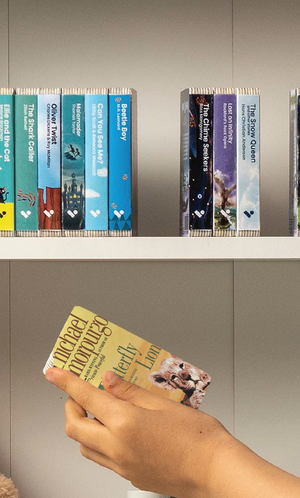A hand taking The Butterfly Lion audiobook from a shelf of Voxblock audiobooks