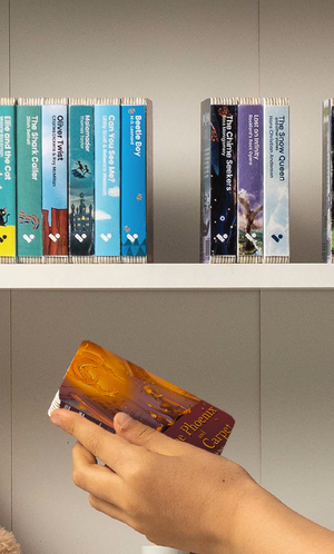 A hand taking The Phoenix and the Carpet audiobook from a shelf of Voxblock audiobooks