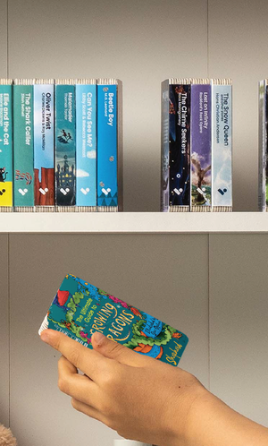 A hand taking The Ultimate Guide to Growing Dragons audiobook from a shelf of Voxblock audiobooks