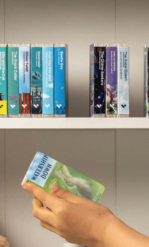 A hand taking the Watership Down audiobook from a shelf of Voxblock audiobooks