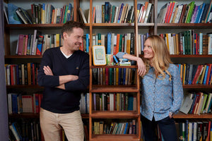 Tom and Rebecca, the Voxblock founders, stand in front of a bookcase, a player and audiobooks on a shelf between them.